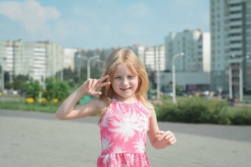 cheerful portrait of a little five year old girl in a pink summer dress on the streets of her city