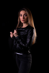 A young girl in a black leather jacket isolated on a black background