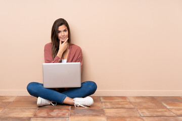 Teenager student girl sitting on the floor with a laptop thinking