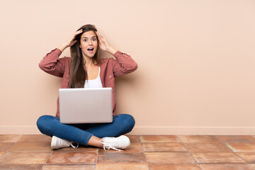 Teenager student girl sitting on the floor with a laptop with surprise expression