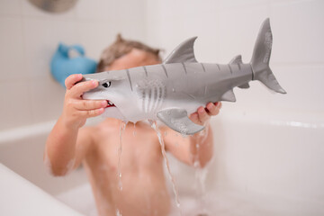 Boy playing in bath with toys and shark toy fish 