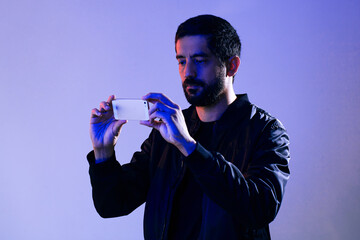 Man wearing jacket and holding cell phone illuminated by blue and red lights. Concept of man...