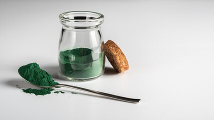 Spirulina Chlorella algae powder in a glass jar and in a spoon on a white background. Horizontal orientation. Scientists are developing research on algae. Bio-energy, biofuel, energy research.