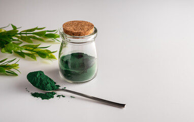 Spirulina Chlorella algae powder in a glass jar and in a spoon on a white background. Horizontal...