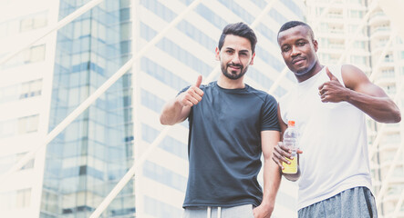 Naklejka premium Happy two handsome muscular athletes stand and showing thumb up with city background.