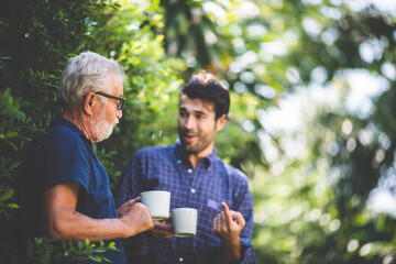 An adult hipster son and senior father talking at home, morning nature scene in the home garden...