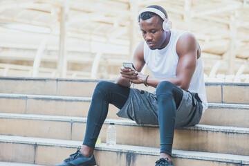 Fototapeta na wymiar Young male athletes sitting on stairs using a smartphone And wearing headphones to listen to music.