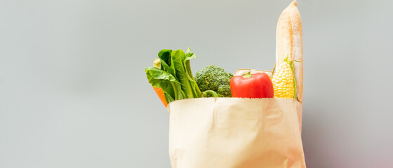 Close up paper bag full of groceries with fresh vegetables and fruit on grey background with copy space. Shopping concept © Patcharanan