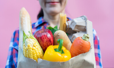 Close up smiling asian woman carrying grocery shopping bag full of fresh vegetables and fruit. Female holding paper bags full of groceries.