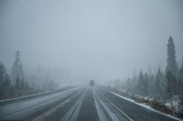 Car driving in heavy snow on highway in pine forest at Banff national park