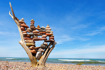 stack of multicolored balanced stones on an old wooden snags, on a blue sky and sea background