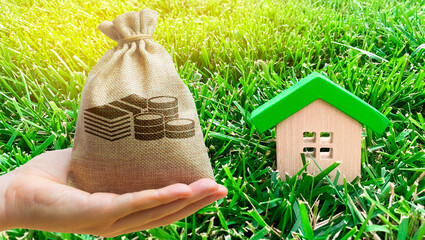 Miniature wooden house and money bag on grass. Real estate concept. Eco-friendly and energy...