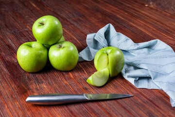High angle shot of some green apples and a knife and a tablecloth on a wooden surface