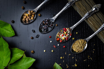 Metal spoons with spices and herbs on a dark background