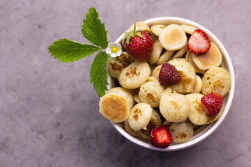 Tiny pancakes with strawberries, quick breakfast, pancake porridge on a gray background, flat lay