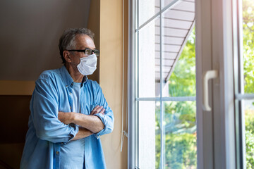 Senior man with protective face mask looking out of window
