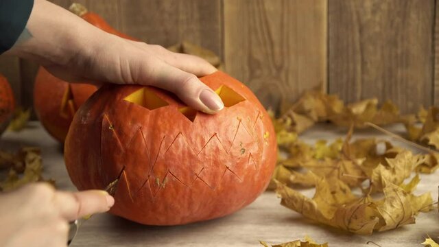 Making a lantern on Halloween from a pumpkin cutting out a toothy mouth with a knife. Theme of traditional Hobbies in autumn and cutting out lanterns. Mystical traditions in Halloween decorations.