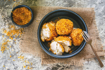 Fried white ice cream on blue plate, grey textured table with textile. Natural day light in the kitchen. Homemade dessert, rustic or country style. Copy space. Hot ice in corn breading. Top view.