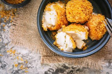Fried white ice cream on blue plate, grey textured table with textile. Natural day light in the kitchen. Homemade dessert, rustic or country style. Copy space. Hot ice in corn breading. Top view.