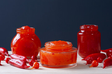 .Transparent glasses of pepper jam on wooden table. Space for text