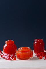 .Transparent glasses of pepper jam on wooden table. Space for text