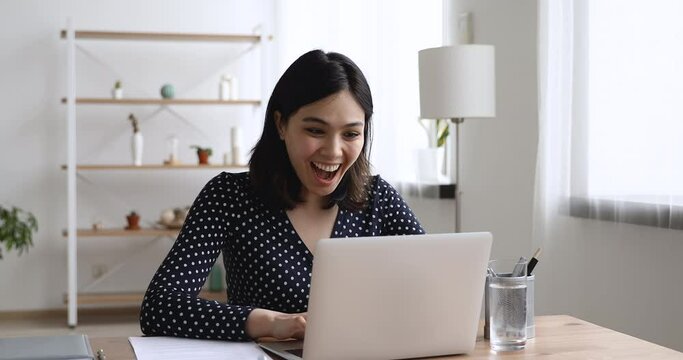 Happy asian young woman sit at desk at home or workplace typing on laptop receive great news celebrating moment of victory, personal achievement, got hired, high school scholarship admission concept
