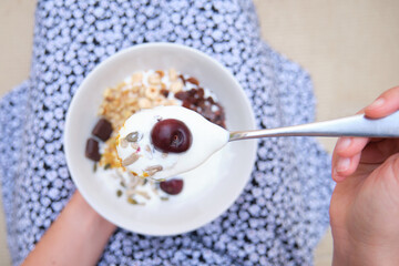 Unrecognizable woman with a cereal, yogurt, fruit bowl and spoon in focus