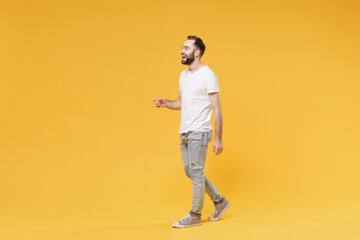 Fototapeta na wymiar Side view fo cheerful young bearded man guy in white casual t-shirt posing isolated on yellow background studio portrait. People emotions lifestyle concept. Mock up copy space. Walking, looking aside.