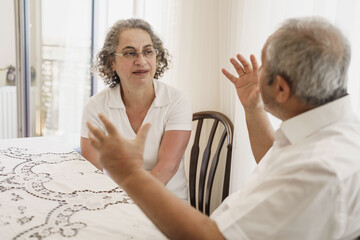Obraz premium Happy elderly couple, quarantined, sitting alone at home, chatting and laughing.