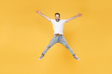 Fototapeta na wymiar Cheerful young bearded man guy in white casual t-shirt posing isolated on yellow background studio portrait. People emotions lifestyle concept. Mock up copy space. Jumping spreading hands and legs.