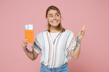 Smiling girl in striped shirt isolated on pink background. Passenger traveling abroad to travel on weekends getaway. Air flight journey concept. Hold passport ticket pointing index finger aside up.