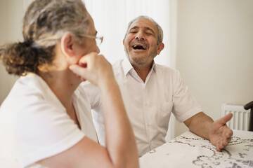 Fototapeta premium Happy elderly couple, quarantined because of covid-19, sitting together at home, chatting and laughing.
