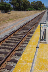 Perspective view of the yellow edge of a railroad platform and the tracks leading into the distance