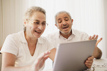 The elderly couple trying to use the tablet show each other something on the screen. old couple is trying to talk to their grandchildren. elders enjoying with benefits of technology