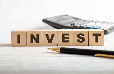 INVEST is written on wooden cubes between a pen and a calculator. Business concept