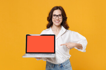 Fototapeta na wymiar Smiling young business woman in white shirt glasses isolated on yellow background studio. Achievement career wealth business concept. Point index finger on laptop pc computer with blank empty screen.