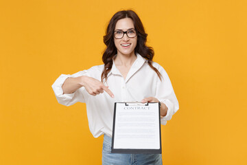 Smiling young business woman in white shirt glasses isolated on yellow background. Achievement career wealth business concept. Mock up copy space. Point index finger on clipboard with papers document.