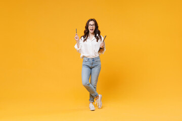 Fototapeta na wymiar Excited young business woman in white shirt glasses isolated on yellow background. Achievement career wealth business concept. Hold clipboard with papers document, pointing pen up with great new idea.