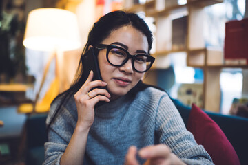 Pretty Asian woman sitting in living room chatting on smartphone