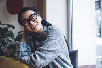 Delighted Asian woman chilling on windowsill at home