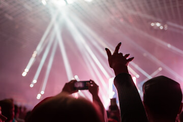 A crowd of people at the concert have fun and dance to the music at the concert. Pink light in background. The concept of entertainment and relaxation