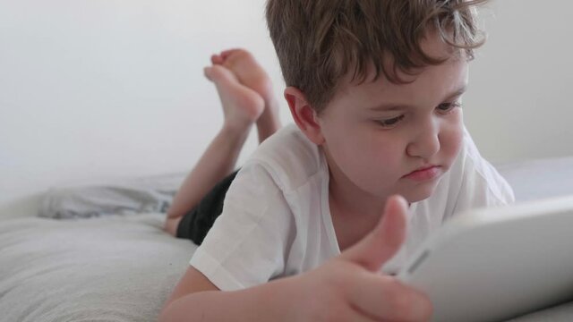 Child watching cartoons on a tablet while lying at home