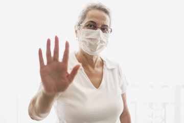 Isolated shot of old woman wearing mask showing stop sign with his open palm, saying that you better stay away from her. keeping hands in stop gesture, saying Stay away from me.