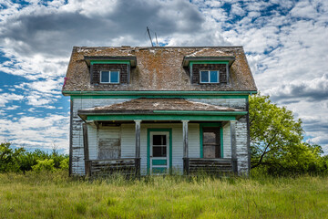 Old, abandoned prairie farmhouse with trees, grass and blue sky in Saskatchewan, Canada