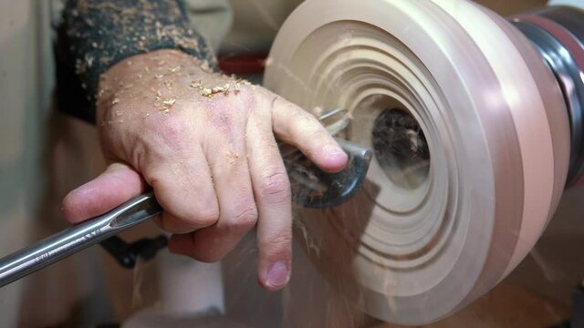 Craftsman works with workpiece in authentic workshop. Woodworker handles wood by bench. Making beautiful wooden handmade dish. Creation of unusual plate. Carpenter cuts wood by graver in soft focus