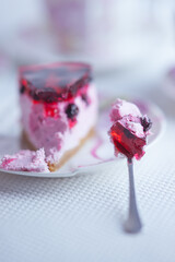 A slice of red currant cheesecake in a saucer with a spoon on a white table. Side view.
