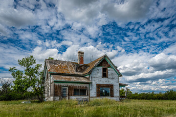 Old, abandoned prairie farmhouse with trees, grass and blue sky in Saskatchewan, Canada