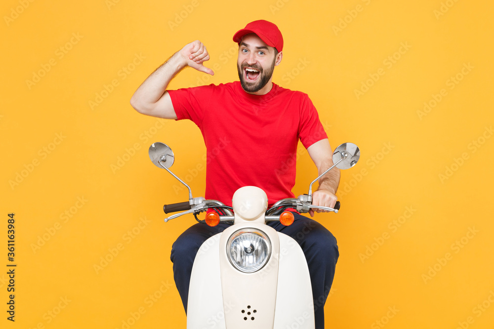 Wall mural Delivery man in red cap t-shirt uniform driving moped motorbike scooter isolated on yellow background studio Guy employee working courier Service quarantine pandemic coronavirus virus covid-19 concept