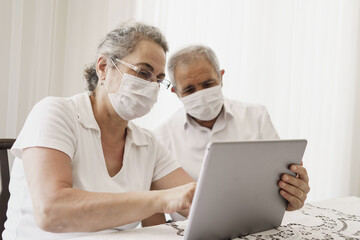 Senior couple wearing medical face mask and using tablet at home. quarantine. Corona Virus. order of products online and communicates on the Internet at home. stay home concept