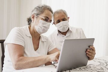 Senior couple wearing medical face mask and using tablet at home. quarantine. Corona Virus. order of products online and communicates on the Internet at home. stay home concept